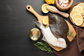 Seafood. Fresh raw flounder fish, spices and juicer on black wooden table, flat lay. Space for text