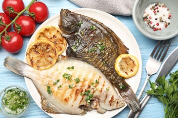Tasty roasted flounder fish with herbs and lemon slices served on light blue wooden table, flat lay. Homemade seafood dish