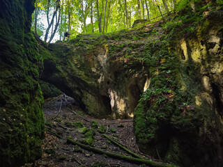The moss-covered rock arch at the entrance of Dante's Hell Cave (Udvar-kő) seen from deep inside,...