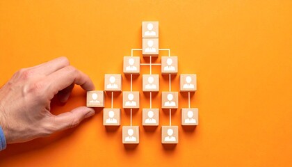 A hand arranging wooden blocks with people icons, symbolizing a hierarchical structure against an orange background.