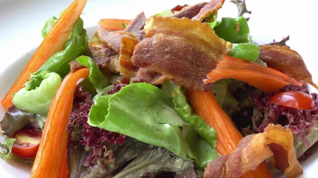 Fresh salad with bacon, crab sticks, and vegetables on a white plate