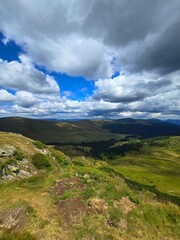 Fototapeta premium Beautiful alpine view over the valley and Parang Mountains from the Transalpina Road viewpoint on a summer day. Rocky cliffs, green grass under a blue sky with dark clouds. Valcea, Romania 