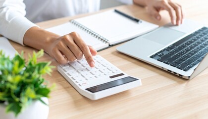 Person using a calculator while working at a desk with a laptop and notebook. The image depicts a workspace environment.