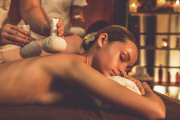 Hot herbal ball spa massage body treatment, masseur gently compresses herb bag on couple customer...