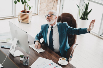 Mature businessman relaxing at his desk in modern office while expressing confidence and positivity