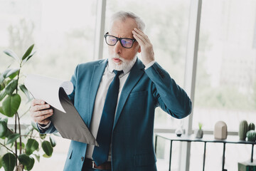 Mature Businessman Reacting with Surprise to Document While Standing in Contemporary Office Setting
