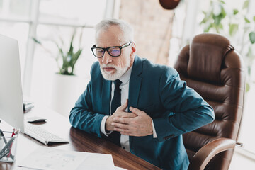 Elderly businessman experiencing health issue in office setting, emphasizing workplace stress...