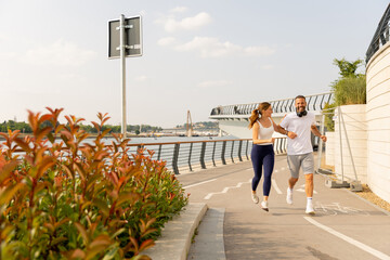 Couple enjoying a lively run along a scenic waterfront path in summer