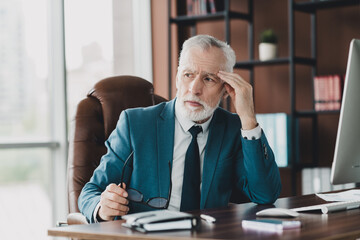 Mature professional businessman reflecting on work decisions in modern office with computer and...