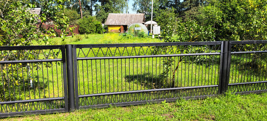 Fenced garden in a serene countryside with a small cottage and greenery