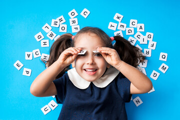 fille souriante avec des couettes entourée de lettres sur un fond bleu