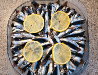 A glass dish filled with rice pilaf and fresh anchovies, neatly arranged and garnished with lemon...