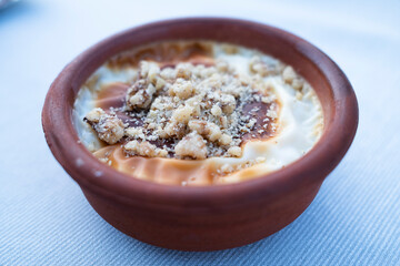 A delicious dessert featuring rice pudding with caramel and crushed nuts, served in a traditional clay pot on a textured tablecloth.