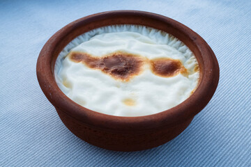 Rice pudding in a traditional clay bowl, showcasing a smooth texture with slight caramelization on the surface, set against a simple backdrop.