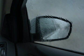 Rearview mirror of a dark gray SUV in rainy weather, drops of water