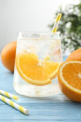 Sparkling water with orange slices in glass, fresh fruits and straws on light blue wooden table, closeup