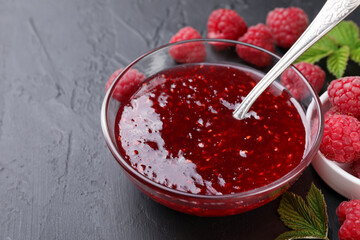 Sweet raspberry jam in glass bowl and berries on gray textured table, closeup