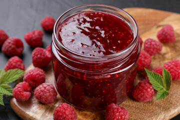 Sweet raspberry jam in glass jar and berries on gray table, closeup