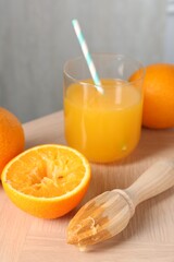 Fresh orange juice in glass, fruits and juicer on wooden table, closeup