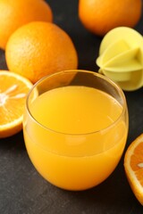 Fresh orange juice in glass, fruits and juicer on black table, closeup
