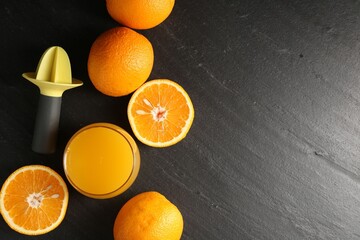 Fresh orange juice in glass, fruits and juicer on black table, flat lay. Space for text