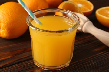 Fresh orange juice in glass, fruits and juicer on wooden table, closeup