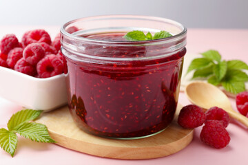 Sweet raspberry jam in glass jar, berries and mint on pink wooden table, closeup