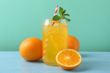 Sparkling water with orange slices in glass, fresh fruits and mint on light blue wooden table against turquoise background