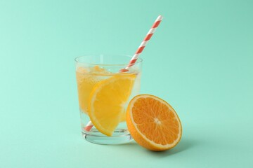 Sparkling water with orange slices in glass and fresh fruit on turquoise background