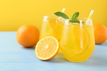 Refreshing soda water with orange slices in glasses, mint and fresh fruits on light blue wooden table, closeup