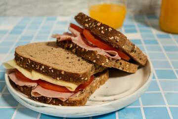 Two delicious sandwiches with wholemeal bread, ham, cheese and tomato slices resting on a white plate