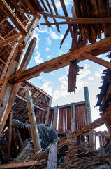 A unique perspective shot from inside a derelict barn, showing the dramatic collapse of the roof with a bright blue sky visible through the gaps.