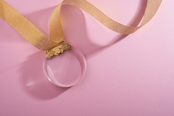 crystal medal with gold ribbon against pink background