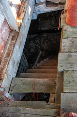 A high-angle shot looking down a steep, narrow set of weathered wooden stairs into a dark,...