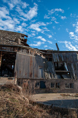 A large, old, abandoned barn with a collapsing roof and damaged walls, with a bright blue sky and...