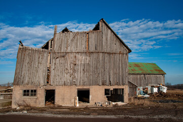 A wide shot of a large, dilapidated barn featuring a decaying wooden upper section and a concrete...
