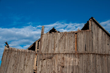A dramatic, low-angle shot of the deteriorating wooden side of an old barn, with its roofline...