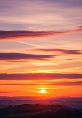 Naklejka premium Vibrant Sunrise Over Rolling Hills - Stunning sunrise landscape with vibrant orange and purple hues, showcasing a sun rising above rolling hills and a hazy horizon