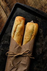 Two fresh baked baguettes on a baking sheet and wrapped in brown paper tied with twine.