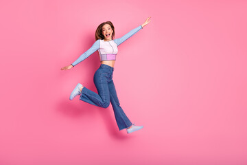 Charming young woman in casual trendy attire joyfully jumping against a vibrant pink background