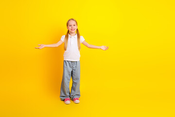 Happy schoolgirl with open arms smiling in front of yellow background representing childhood and education