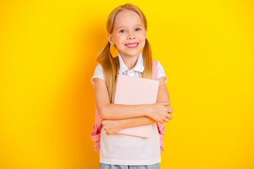 Happy schoolgirl holding a pink notebook with a yellow background promoting education and childhood learning concepts
