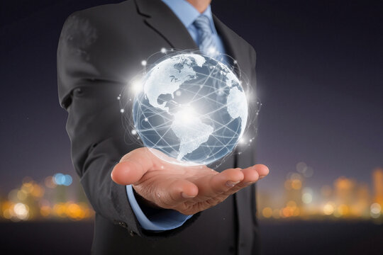 Businessman in dark suit holding glowing digital globe network hologram against blurred city background