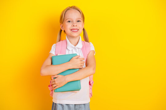 Smiling schoolgirl holding book with yellow background emphasizing youthful enthusiasm and education