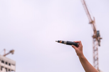 Man holding a cross section of a power cable, showing its layers and wiring against construction background, concept of urban development.