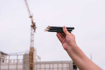 Male hand holding several electrical wires with copper cores. Electrician works on construction...