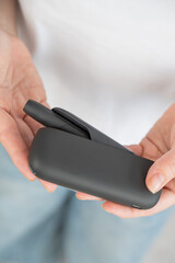 A woman takes a tobacco heating system out of a charger. Electronic cigarette.