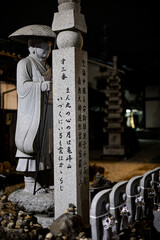 stone statue of a figure with a conical hat and a tall stone pillar inscribed with Japanese...