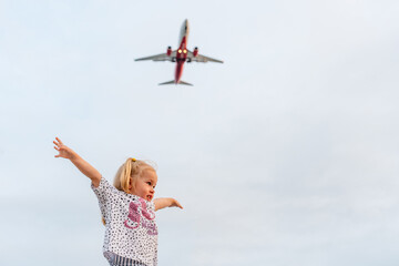 Little child girl looks at a plane in the sky