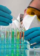 Chemist researcher with protective goggles, mask and gloves, working in lab, dropping liquid in test tubes, closeup detail